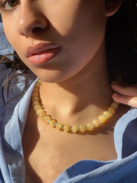 try on shot of the hand-beaded Citrine Skies Necklace No.02 in butter yellow agate stones and tormaline blue stones A soft summer day, captured in stone.Inspired by the golden warmth of citrine sunsets and the tranquility of clear skies. Blends butter yellow and sky blue tones in a dreamy, refreshing palette. Handcrafted with natural jade and tormaline gemstones and finished with 925 sterling silver clasp. Featuring: Material: Natural jade stones - Length: 42 cm - 925 sterling silver clasp
