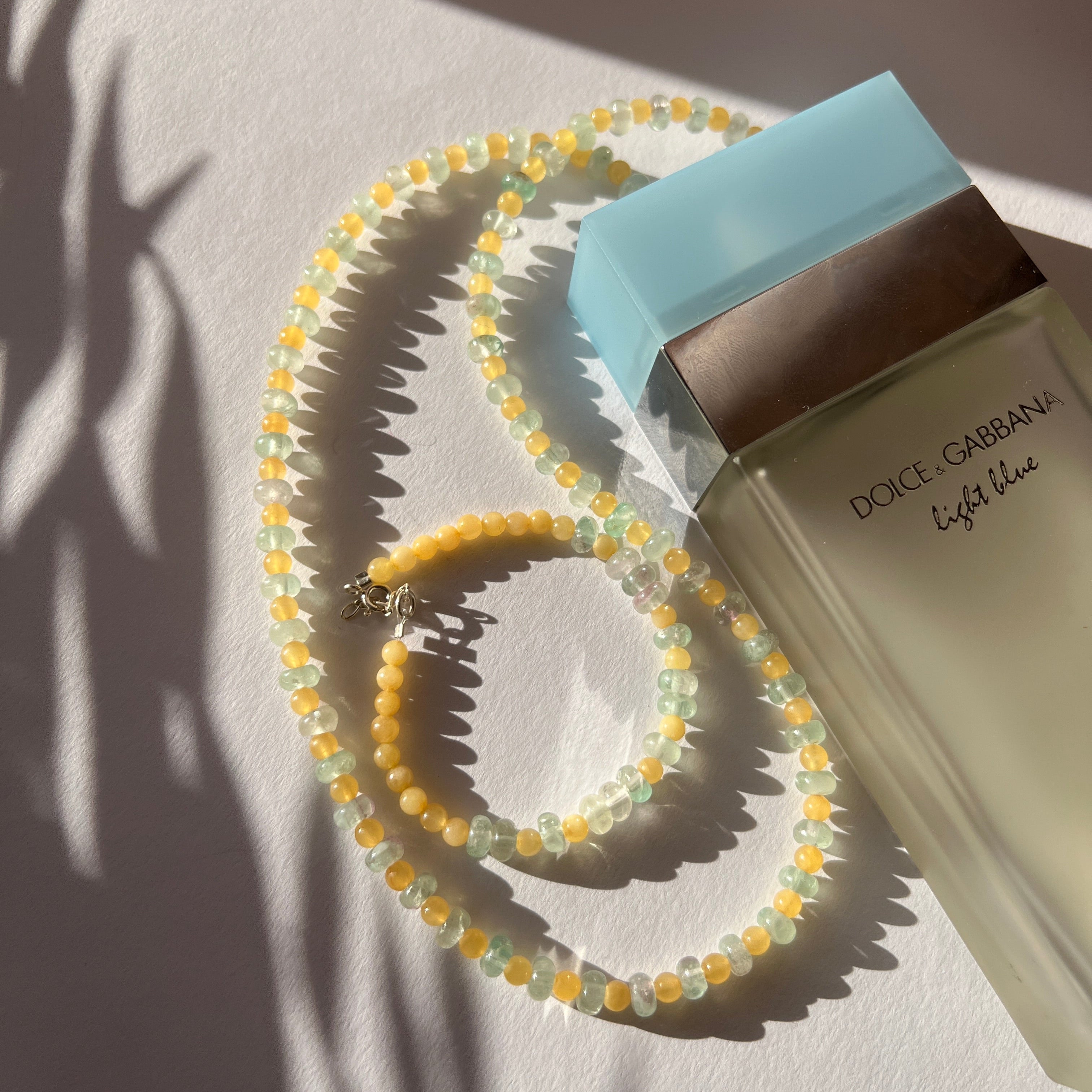 styling a hand-beaded Citrine Skies set of necklace and bracelet in butter yellow agate stones and tourmaline blue stones.
 A soft summer day, captured in stone.
Inspired by the golden warmth of citrine sunsets and the tranquility of clear skies. Blends butter yellow and sky blue tones in a dreamy, refreshing palette. Handcrafted with natural jade and  tourmaline  gemstones and finished with 925 sterling silver clasp.  Material: Natural jade stones - Length: 42 cm - 925 sterling silver clasp. 