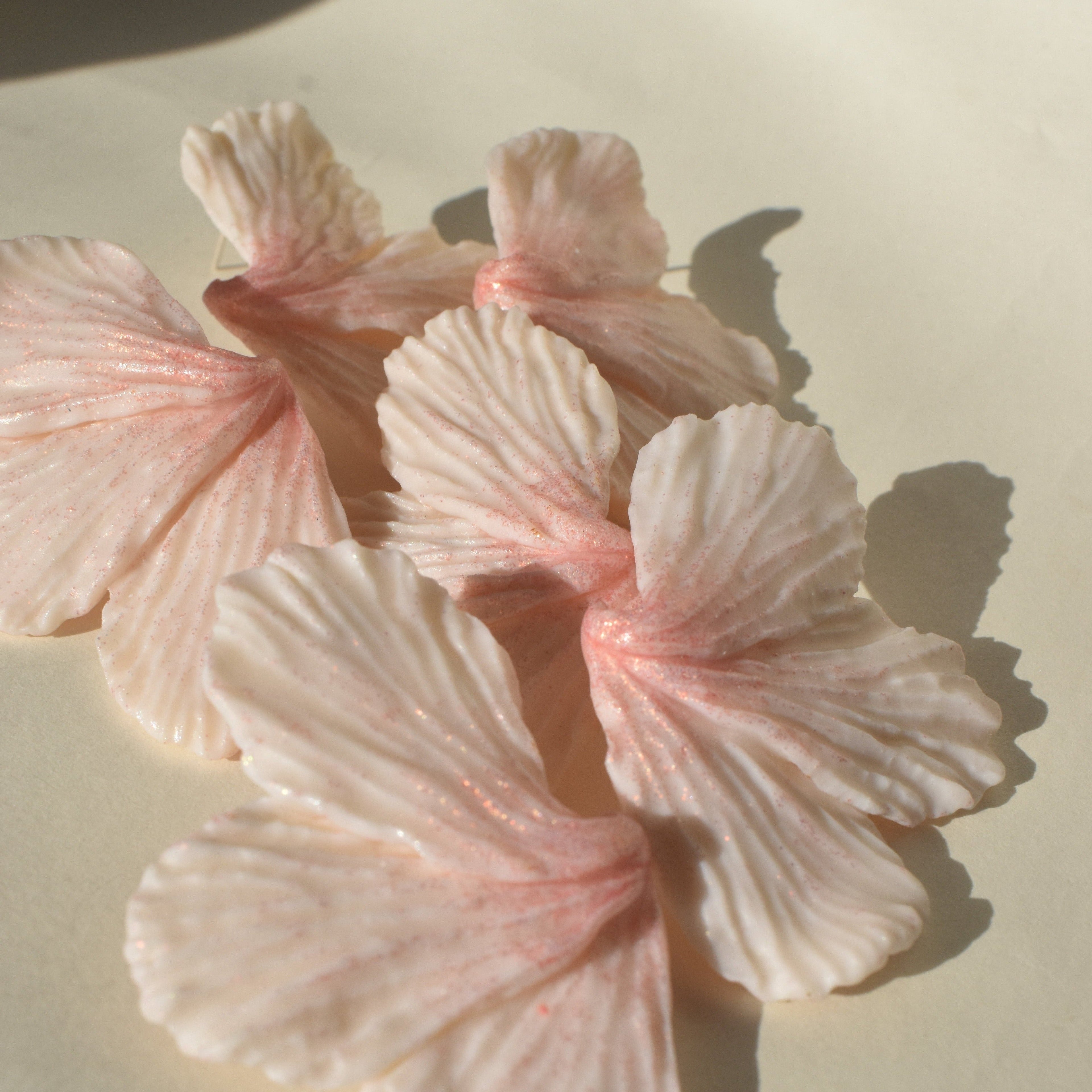 A close-up of pink shimmering lily blossom earrings made from polymer clay with stainless steel posts.