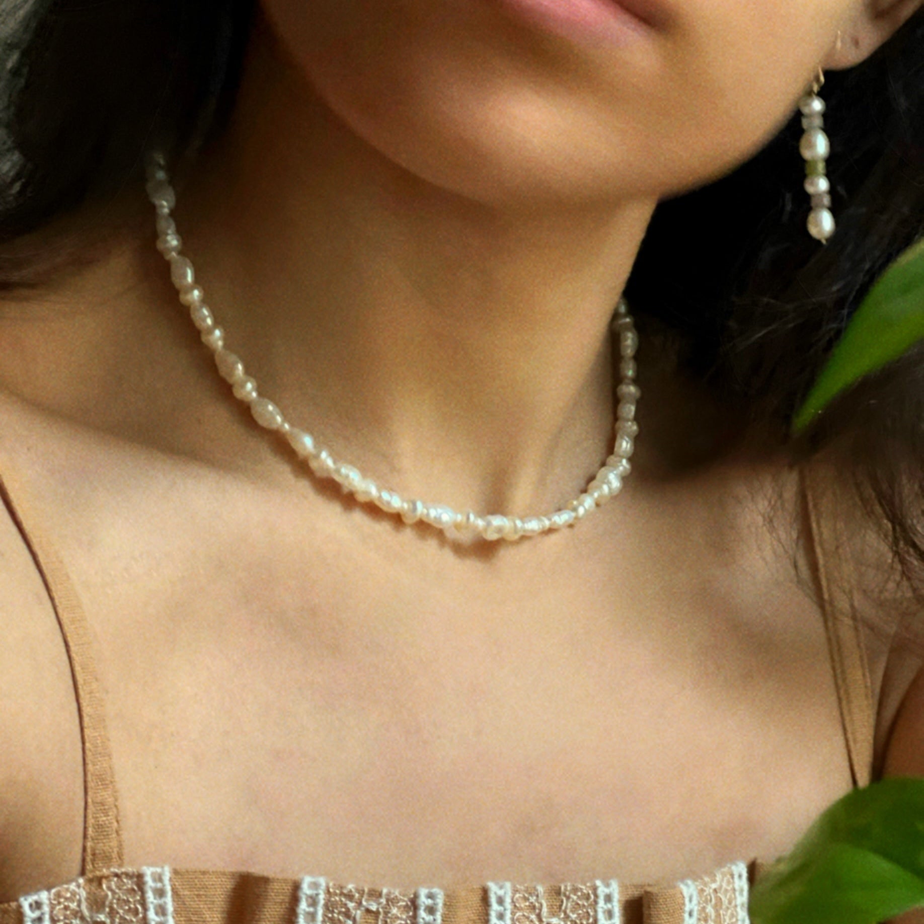 A person wearing a Serene necklace with white pearls and a silver clasp, paired with a casual blouse.