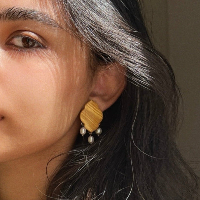 Close-up of a woman wearing a gold earring with dangling pearls.