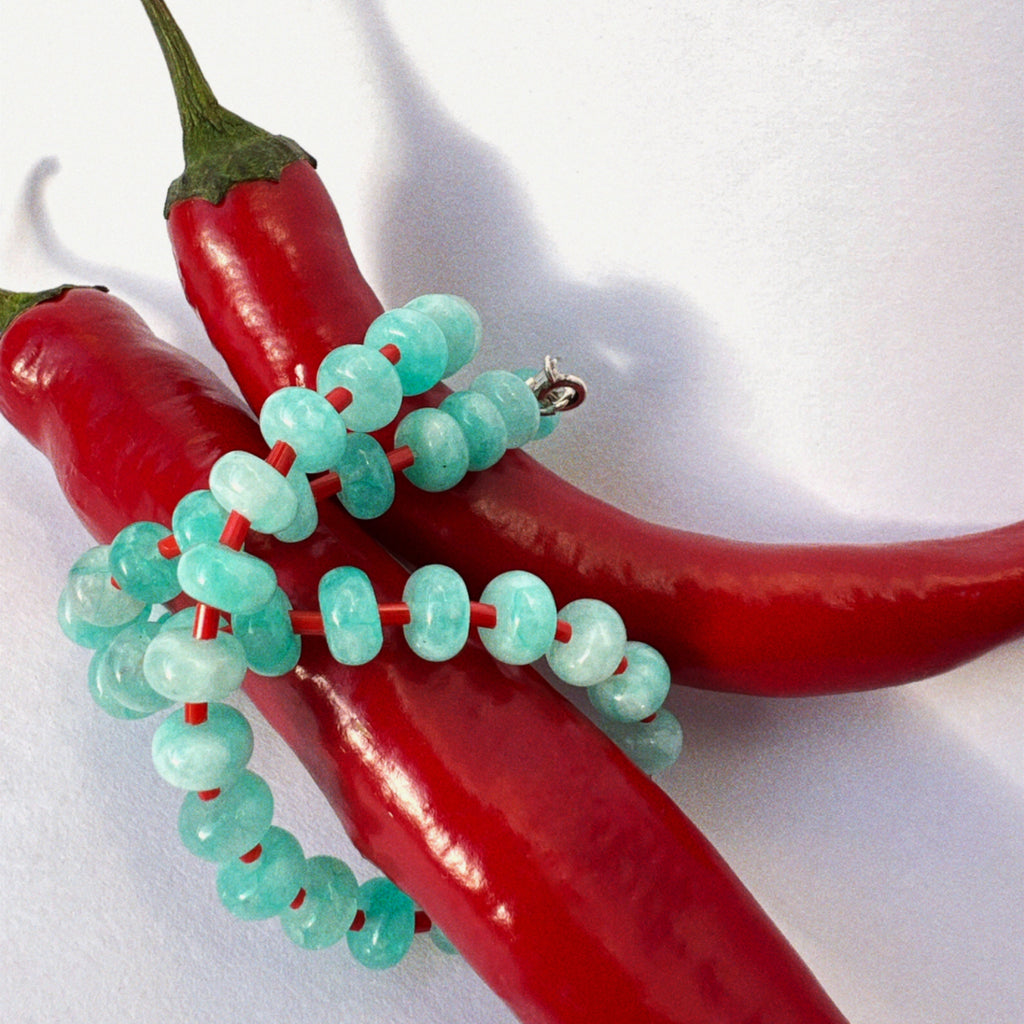 close-up of handmade necklace made using button shaped beads of blue agate stones with tiny red glass beads. trending chunky beaded necklace for summer