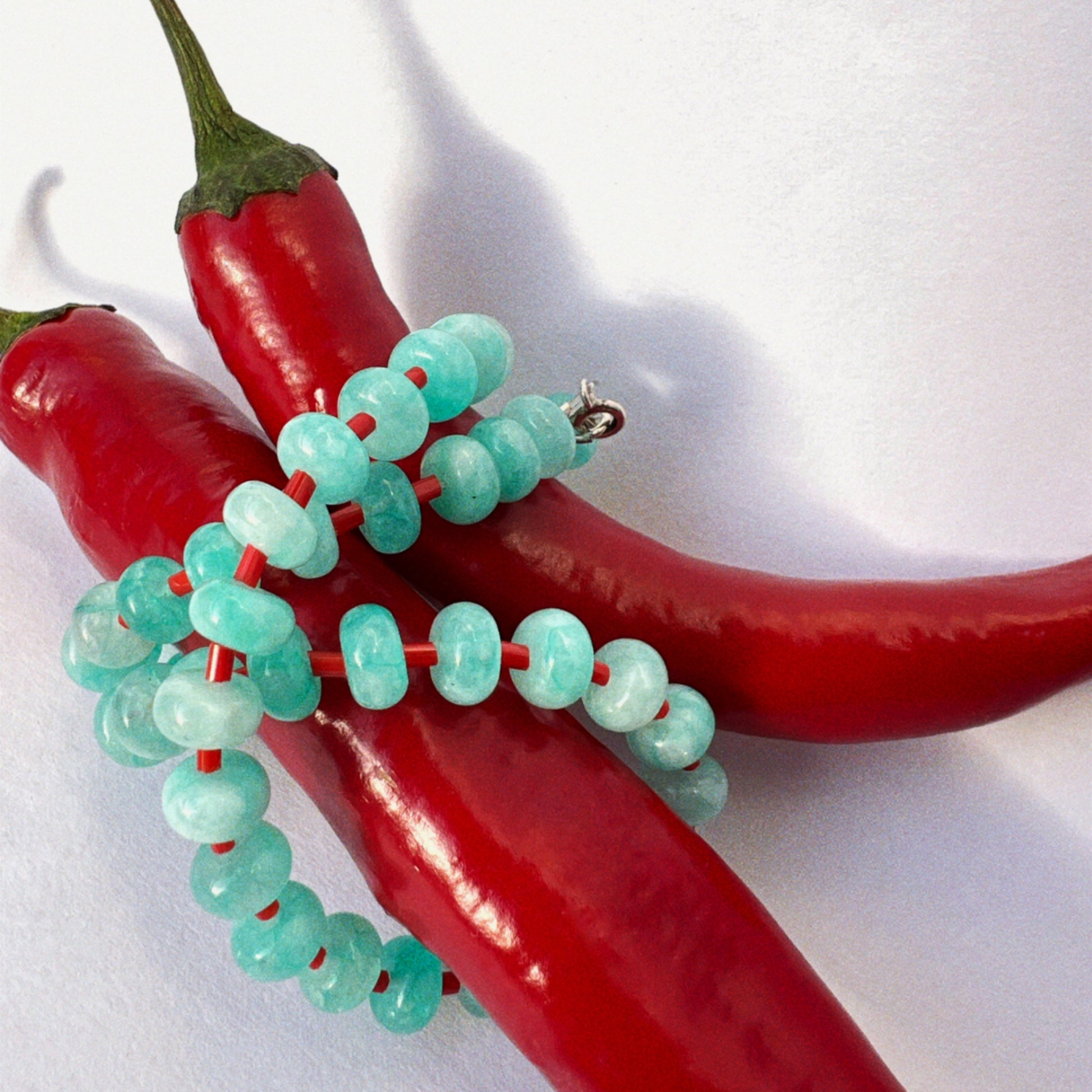 close-up of handmade necklace made using button shaped beads of blue agate stones with tiny red glass beads. trending chunky beaded necklace for summer