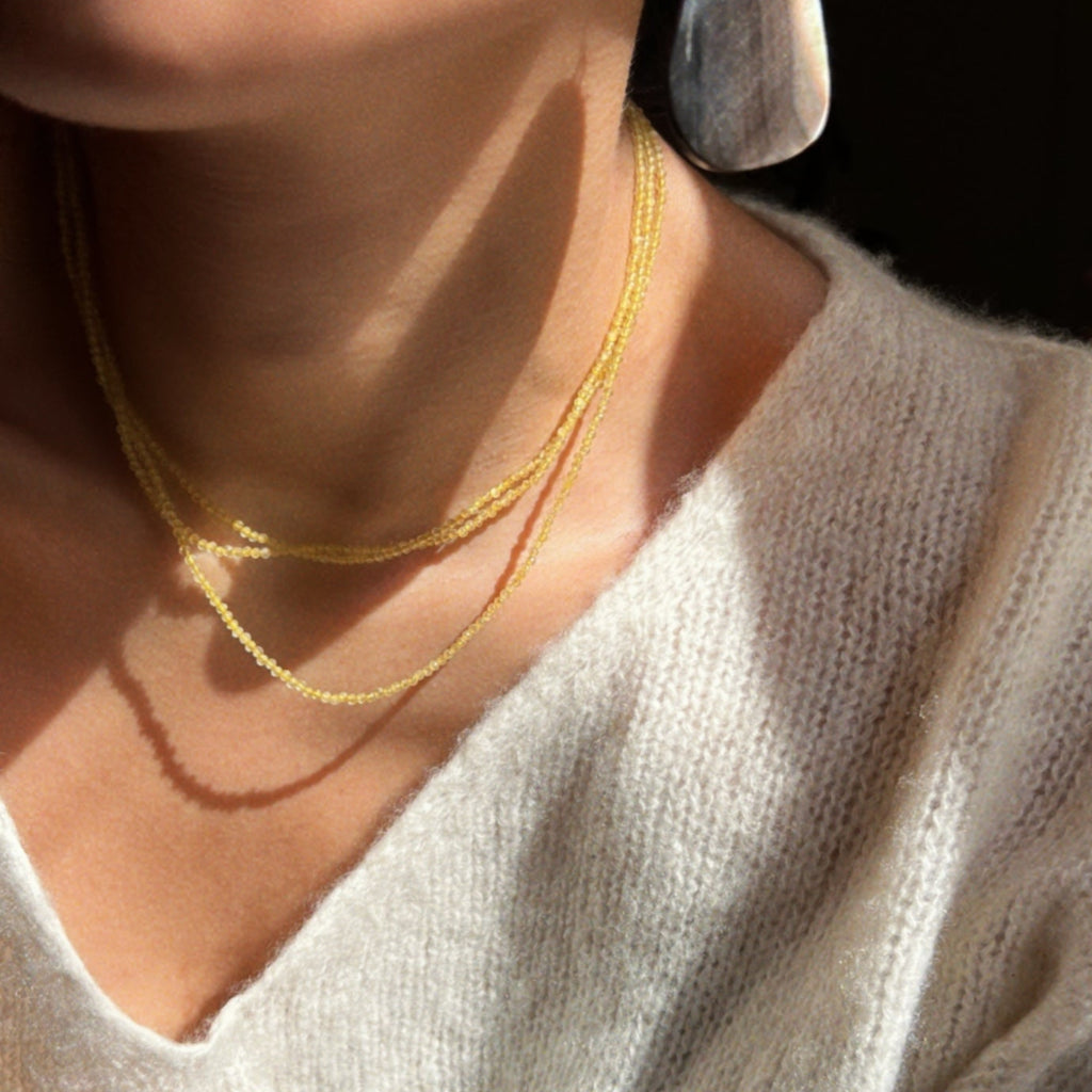 Close-up of shot for yellow three layered necklace and brown shell teardrop earrings.
